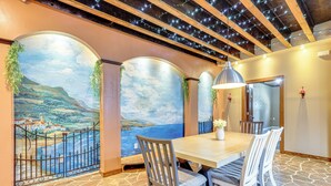 A dining area with a table and chairs, a mural of a coastal scene, and a stone floor. - Italian-Styled Home w/ Lake Views & Private Pool (Belton)
