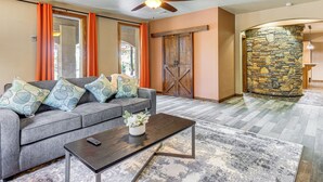 A living room with a gray sofa, orange curtains, a ceiling fan, and a stone wall. - Italian-Styled Home w/ Lake Views & Private Pool (Belton)