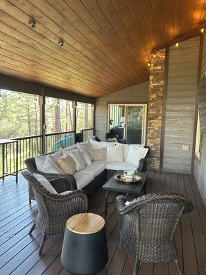 A covered outdoor seating area with a sofa, chairs, and a table, overlooking a forested area.