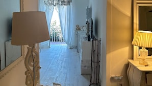 A room with a chandelier, a mirror, a lamp, and a view of a balcony.