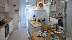 A kitchen with white cabinets, a wooden countertop, and a large mirror. There is a sink, stove, and various kitchen items on the counter.