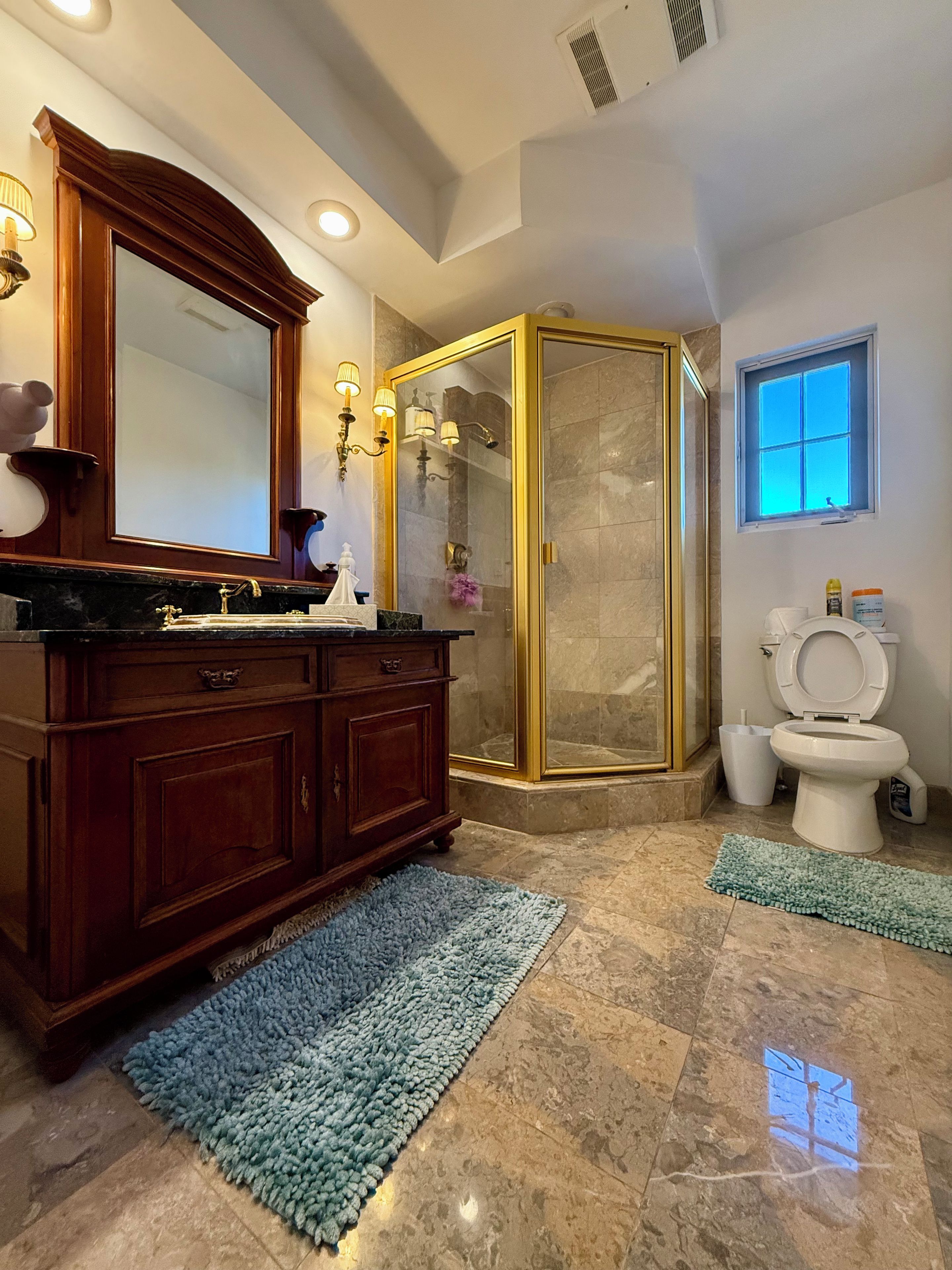 Un bagno con pavimento in marmo, un mobile lavabo in legno, una cabina doccia in vetro, un water e una finestra.