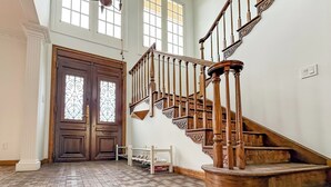 Una habitación espaciosa con una escalera de madera, ventanas amplias y un suelo con estampado de espiga.