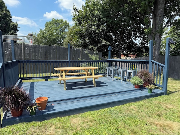 A deck with a picnic table and bar stools, surrounded by a blue railing and potted plants.