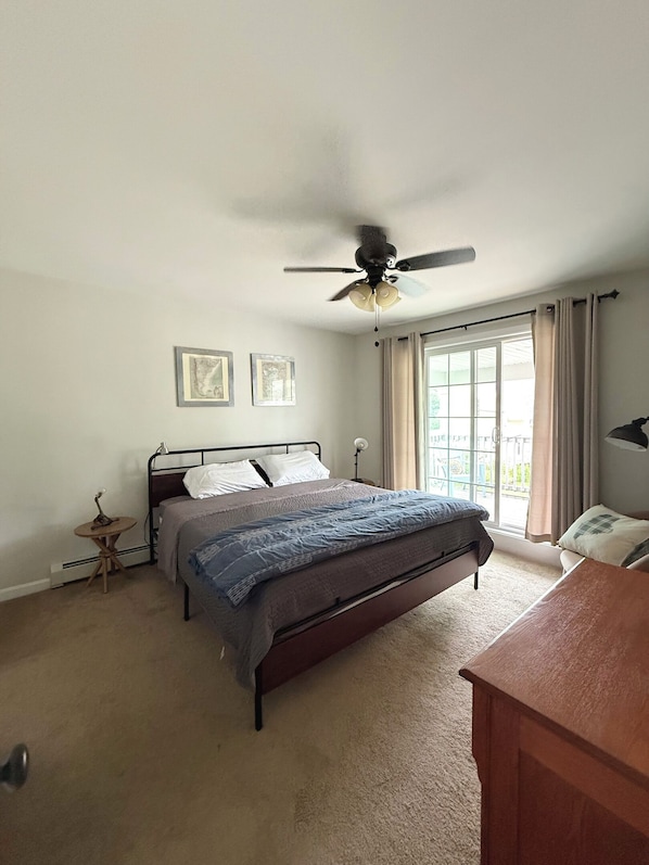 A bedroom with a bed, a ceiling fan, a desk, and a window with curtains.