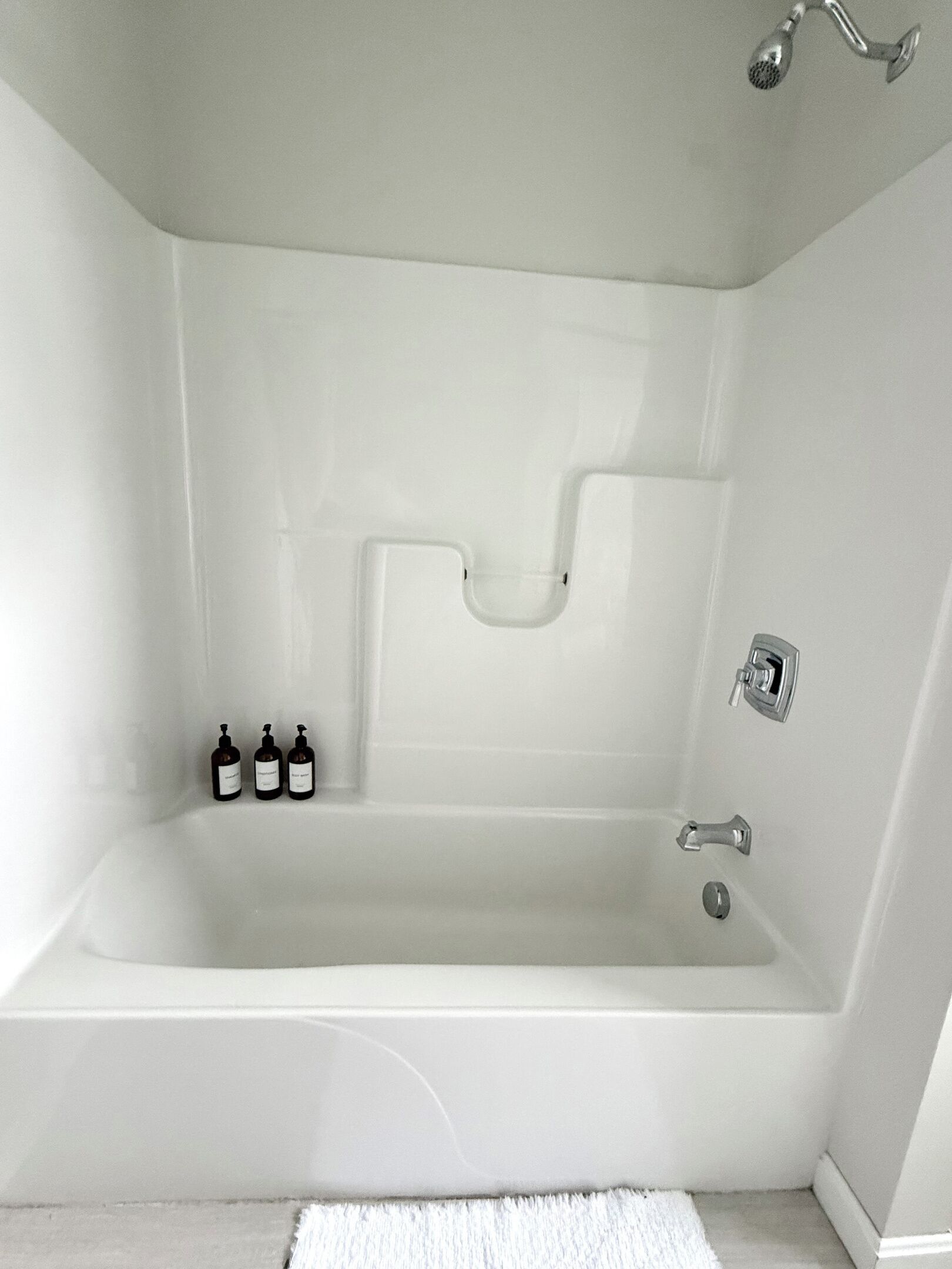 Une baignoire blanche au design moderne, une douchette et trois bouteilles de shampoing.