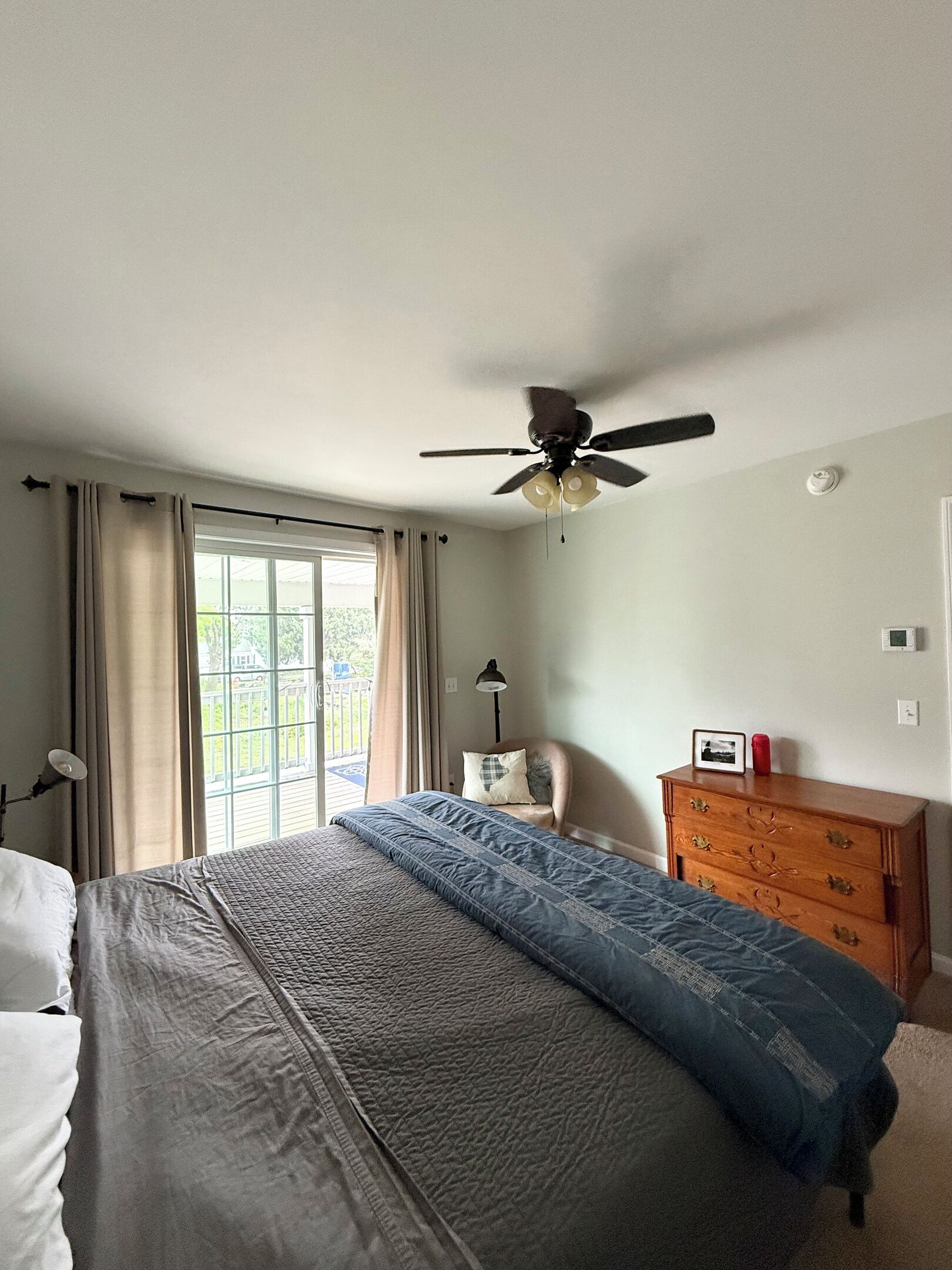 A bedroom with a bed, a ceiling fan, a dresser, and a window with curtains.
