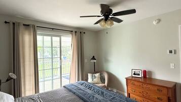 A bedroom with a bed, a ceiling fan, a dresser, and a window with curtains.