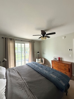 A bedroom with a bed, a ceiling fan, a dresser, and a window with curtains.