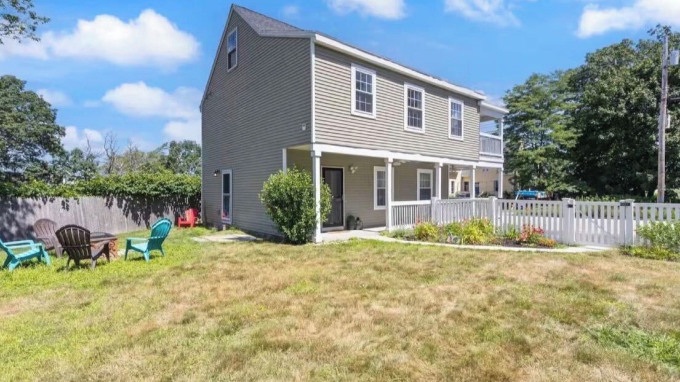 A two-story house with a front porch, a fenced backyard, and outdoor seating.