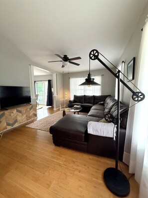 A modern living room with a flat-screen TV, a ceiling fan, a sofa, and a floor lamp.