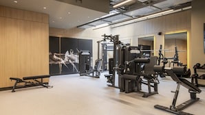Ett modernt gym med olika typer av träningsutrustning, en stor spegel och en TV som är monterad på väggen.