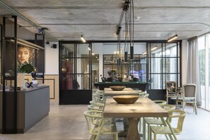 Een modern interieur met een lange houten tafel en lichtgroene stoelen, een zwarte toonbank met een plant en grote ramen voor natuurlijk licht.