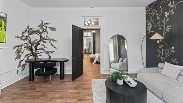 Un salon moderne avec un plancher en bois, une table à manger noire, un canapé gris et un fauteuil noir.