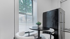 Une cuisine compacte avec un réfrigérateur noir, une petite table ronde avec deux chaises et une plante en pot posée sur la table.