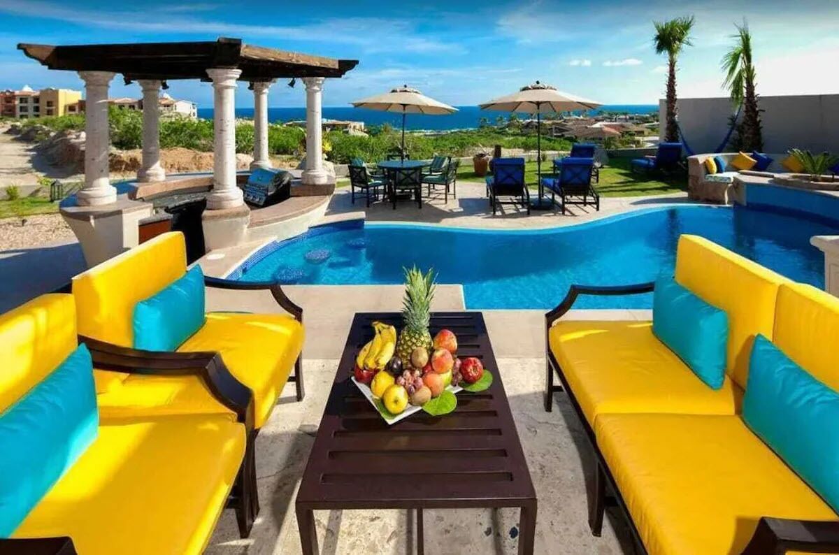 A poolside area with yellow and blue outdoor furniture, a table with fruit, and a view of the ocean.