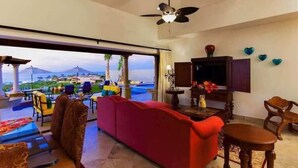 Amplia sala de estar con un sofá rojo, un ventilador de techo y vistas a un resort con palmeras y una piscina.