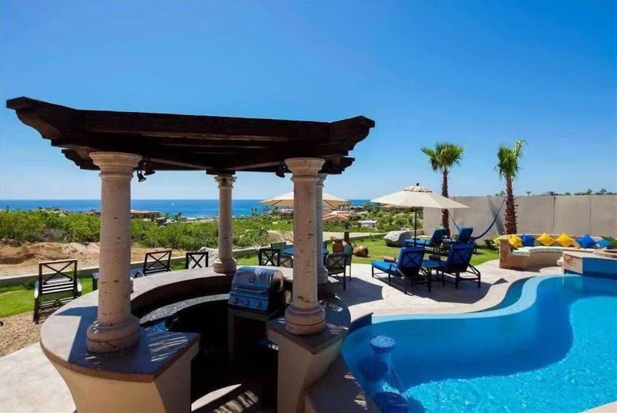 A swimming pool with a pergola, lounge chairs, and a view of the ocean.
