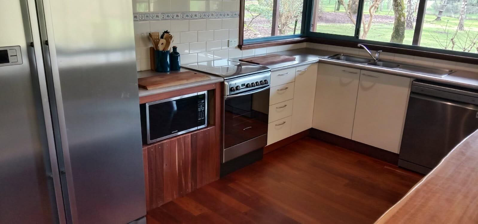 A kitchen with a built-in oven, microwave, and dishwasher, wooden cabinets, and a window with a view of the outdoors.