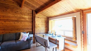 Interior de una cabaña de madera con sofá, banca, mesa de comedor y un ventanal grande.