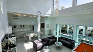 A spacious living area with a pool table, a bar area, and a large window overlooking a pool.