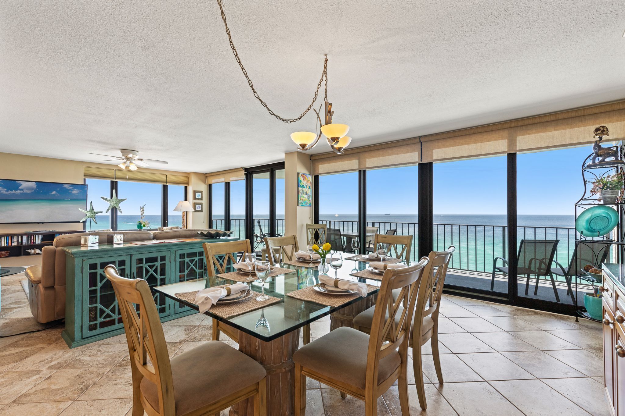 A spacious dining area with a glass table and chairs, a teal-colored kitchen island, and a view of the ocean through large windows.