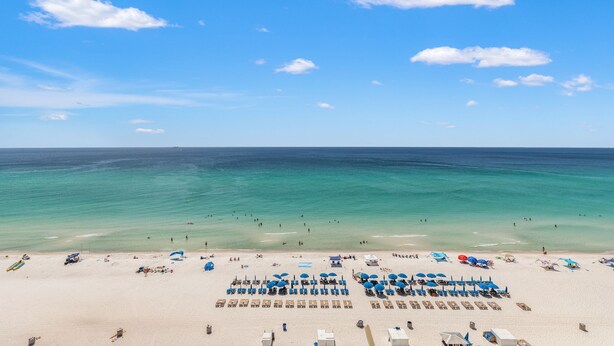 A beach with clear turquoise water, a sandy shore, and several blue umbrellas and sun loungers. - It Doesnt Get Any Better Than This! 2BR 2BA Sleeps 8 Beachfront! (Panama City Beach)