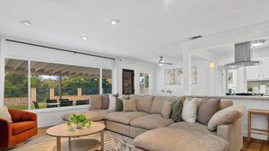 A modern living room with a large sectional sofa, a round coffee table, and a view of the outdoors. - Traveler's Deam Home - SDSU - Hot Tub - Pool Table (San Diego)
