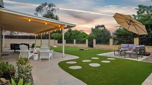 A covered patio area with outdoor furniture, a fire pit, and a well-maintained lawn with stepping stones. - Traveler's Deam Home - SDSU - Hot Tub - Pool Table (San Diego)