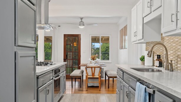 A modern kitchen with grey cabinetry, a wooden dining table, and a view through the window. - Traveler's Deam Home - SDSU - Hot Tub - Pool Table (San Diego)