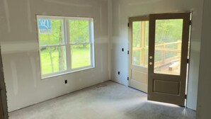 A large, empty room with white walls and a concrete floor, featuring a large window and a door leading outside. - Pet-Friendly Luxury Home w/ Hot Tub and Mountain Views (Franklin)