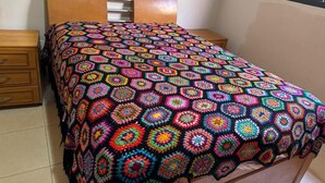A bed with a colorful, patterned blanket, a wooden headboard, and a nightstand with a drawer. - ACCOMMODATION BARRETOS PEÃO FESTIVAL - 2025 (América Barretos)