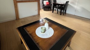 Un salon moderne avec une table basse noire, un téléviseur fixé au mur, un coin repas avec une table et des chaises, et une lucarne.