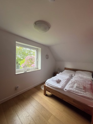 Un dormitorio con ventana, cama, mesita de noche y lámpara de pared.