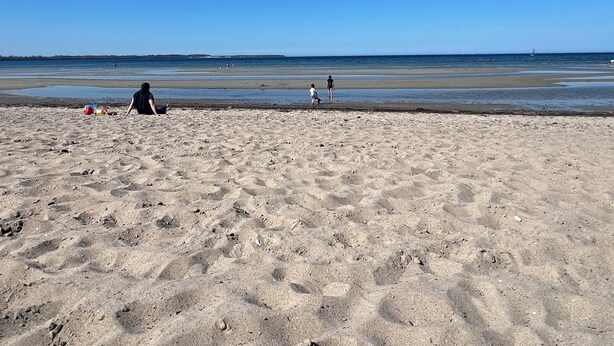 Une plage de sable avec des empreintes, un ciel bleu clair et une mer calme.