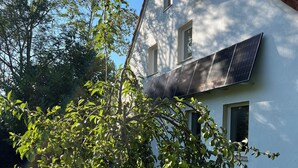Une maison avec des panneaux solaires sur le toit, un arbre dans la cour et un ciel bleu dégagé.