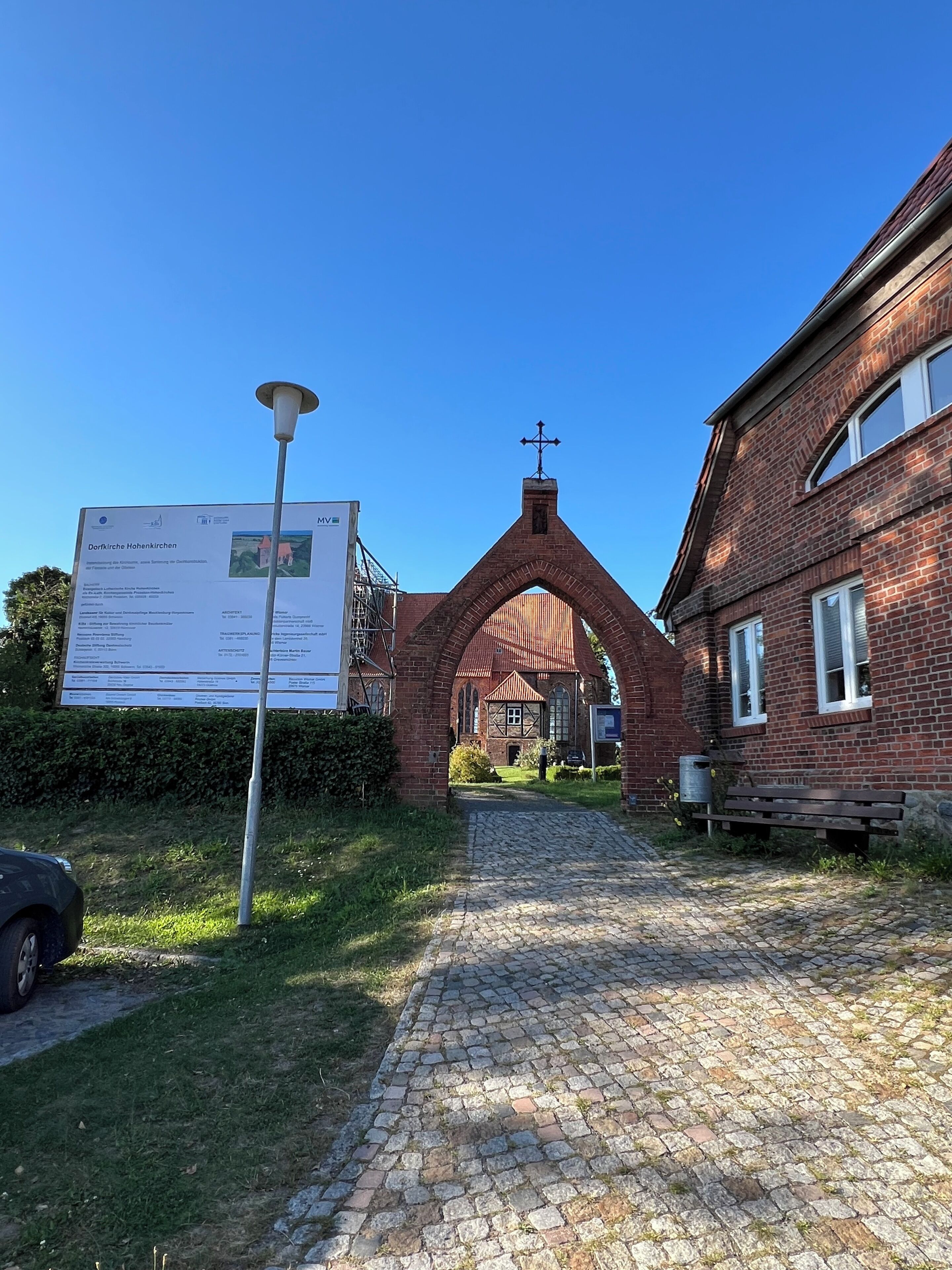A brick building with a large archway entrance, a signboard, and a paved pathway leading to the building.