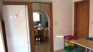 A kitchen with a white refrigerator, wooden cabinets, a dining table with chairs, and a small table with colorful baskets.