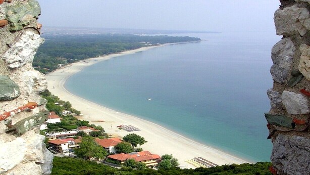 A coastal view from a stone structure overlooking a beach with houses and greenery.