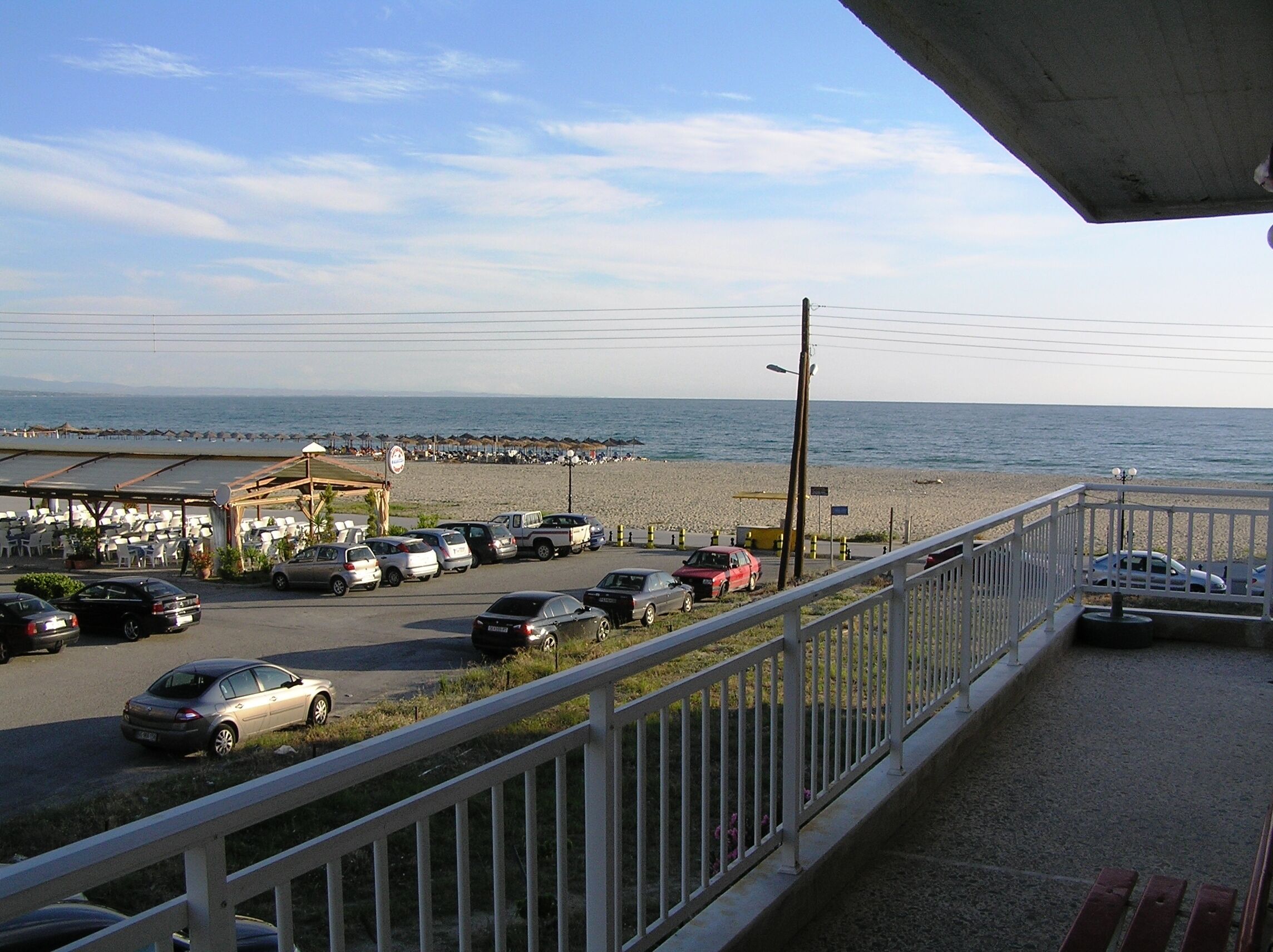 A beachside parking area with cars, a covered seating area, and a view of the ocean.