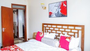 Ein Schlafzimmer mit hölzernem Kopfende, einem Bett mit weißer und rosa Bettwäsche, einem roten abstrakten Gemälde an der Wand und einer Chandelier.