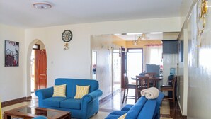 Ein Wohnzimmer mit einem blauen Sofa, einem Couchtisch und einem Essbereich mit Tisch und Stühlen.
