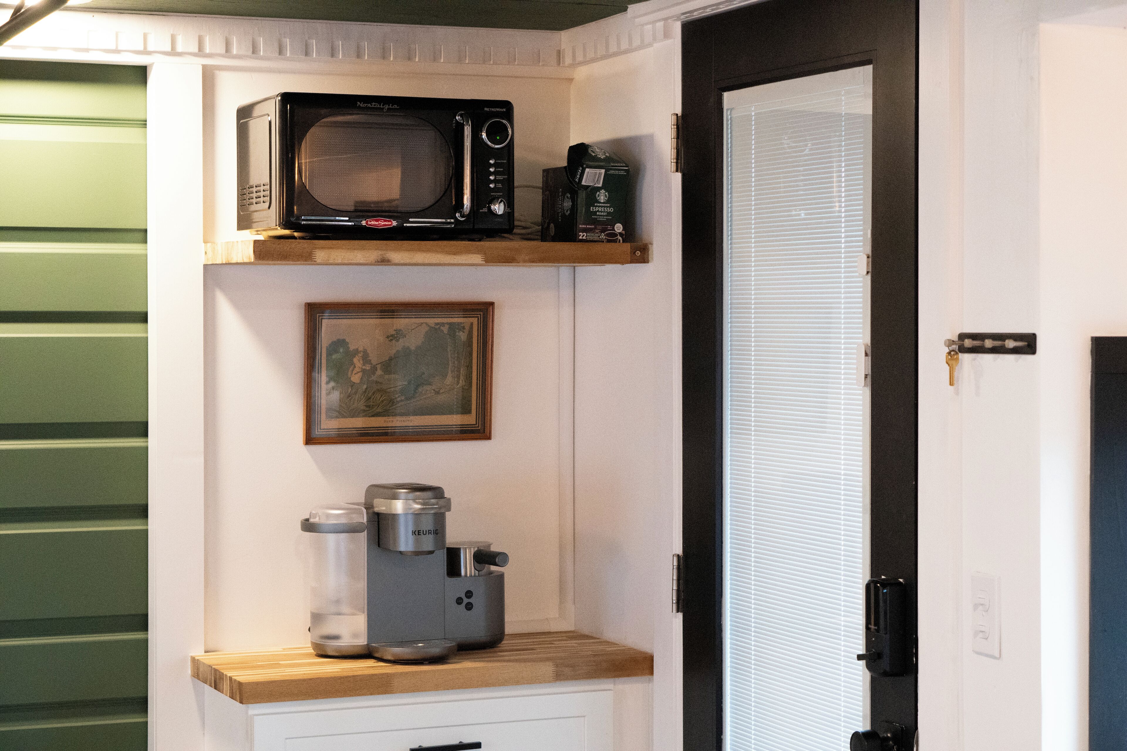 A kitchenette with a microwave, coffee maker, and espresso machine on a wooden countertop.