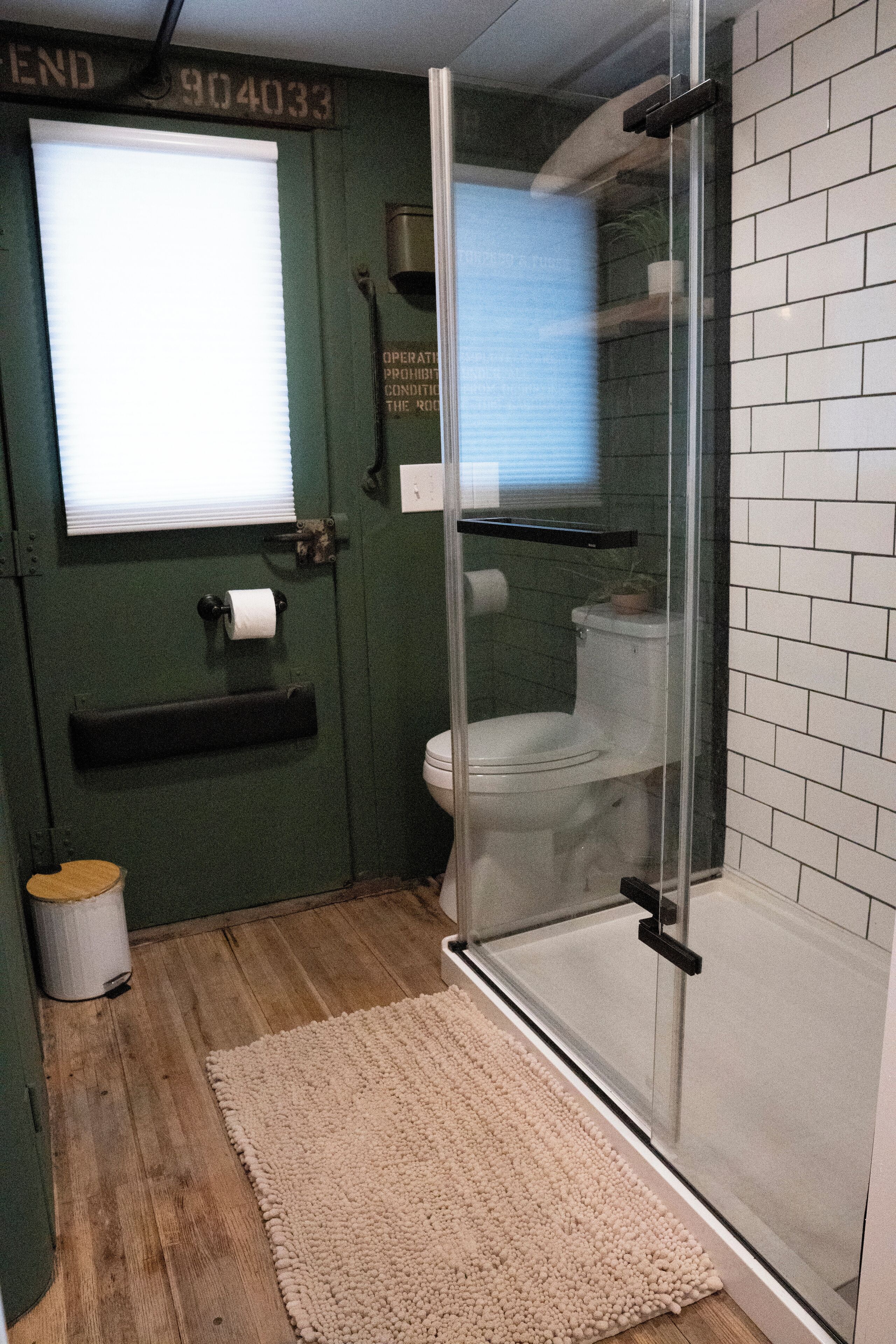 Baño con cabina de ducha de vidrio, inodoro, suelo de madera y alfombra color crema.