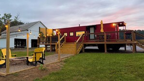 Um deck de madeira com cadeiras Adirondack, um edifício vermelho e uma área coberta com um guarda-sol amarelo.