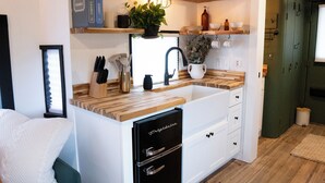 A compact kitchen with a sink, wooden countertop, and a refrigerator. - Caboose Tiny Home in Frazier’s Bottom, WV (Fraziers Bottom)