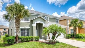 A two-story residential house with a front porch, palm trees, and a well-maintained lawn. - The Minions Mansion 6br Resort Pool Home By Disney (Kissimmee)