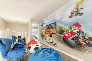 Una habitación temática de carreras, que incluye un mural de Mario Kart, un televisor y un sillón de peluche.