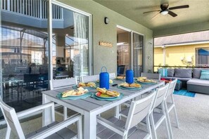 Un área de comedor al aire libre con una mesa lista para una comida, sillas y un ventilador de techo.