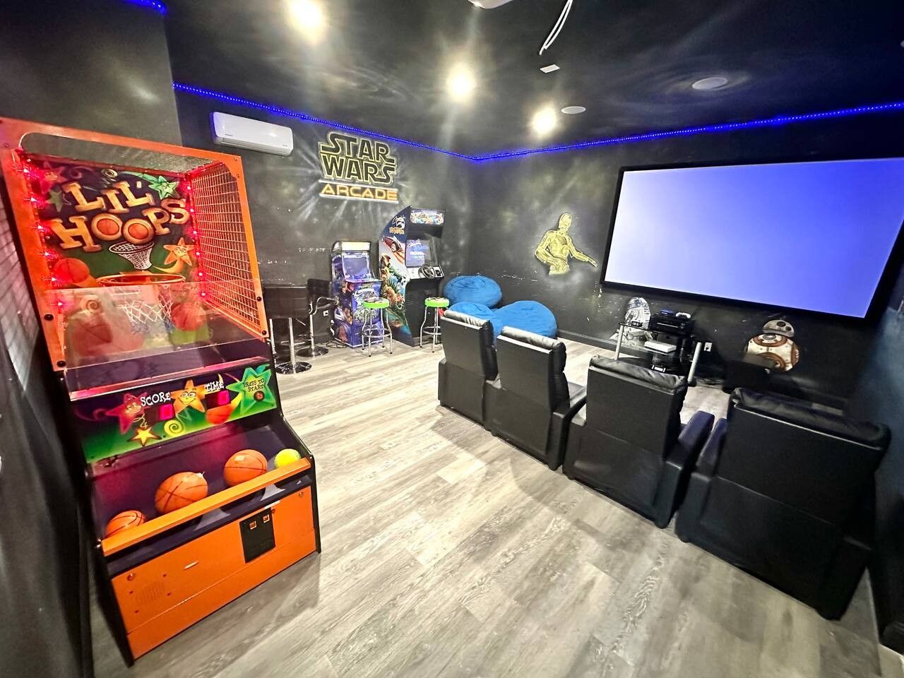 Une salle avec des jeux d’arcade, un grand écran et des espaces aménagés pour s’asseoir.